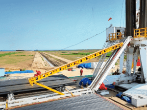 An automatic catwalk deployed on an oil drilling rig, connecting the work area to the derrick; yellow structure clearly visible against an open oilfield landscape.