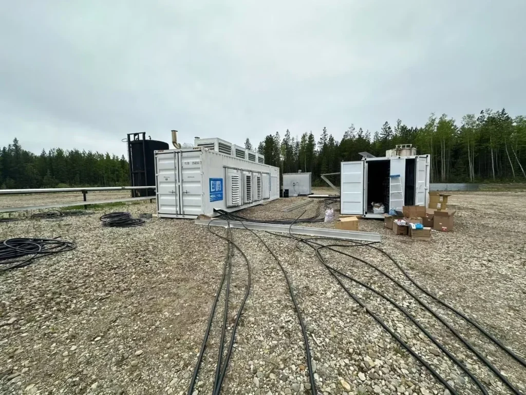 Containerized associated gas CHP power generation unit deployed at oilfield site with cables, white equipment containers, and forest backdrop