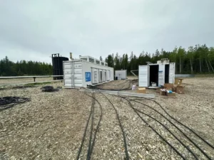 Containerized associated gas CHP power generation unit deployed at oilfield site with cables, white equipment containers, and forest backdrop