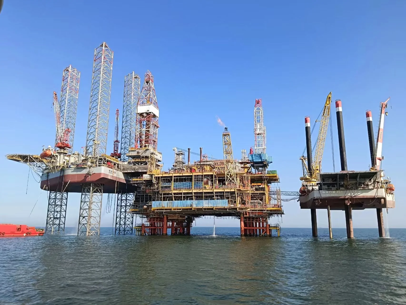 Production platform deck with process modules and flare boom, jack-up rig alongside